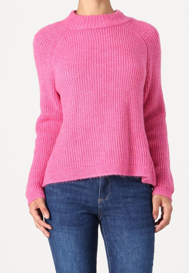 Pull rose tricoté avec un col haut, une texture côtelée et une coupe légèrement ample, assorti à un jean en denim bleu.