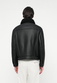 Cazadora de couro preta com colarinho de pelo, design cropped e textura suave. Apresenta punhos com botão e ajustador na cintura nas costas.