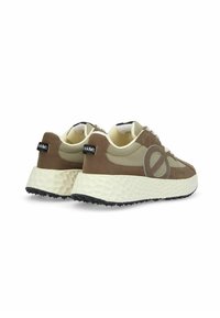 Bruine en beige sneakers met een gestructureerde, chunky zool. Heeft een afgeronde vorm, vetersluiting en een prominent logo aan de zijkant.