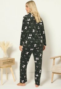 Conjunto de pijama negro con mangas largas y pantalones, que presenta un patrón de lazos rosas y puntos blancos. La tela parece suave con una textura lisa.