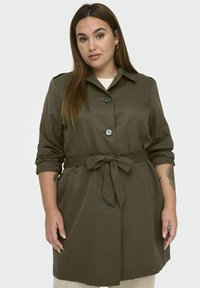 Olivově zelený trench coat s páskem, límcem, třemi knoflíky a ohrnutými rukávy. Má boční kapsy a hladkou texturu látky.