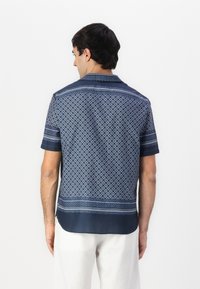 Short-sleeve shirt made of navy fabric, featuring an intricate geometric pattern, subtle texture, and a contrasting patterned neckline and hem.