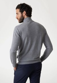 Maglione grigio a maglia con colletto alto e polsini a costine, abbinato a pantaloni blu navy. Texture liscia e design aderente.