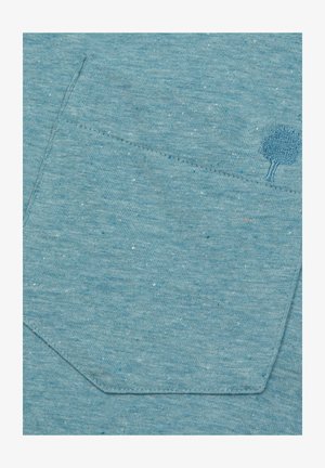 Helles blaues, strukturiertes Gewebe mit einer aufgenähten Tasche und einem dekorativen gestickten Baumdesign sowie dunkleren blauen Sprenkeln.