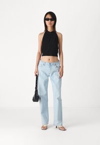 Black halter crop top, light blue high-waisted jeans, black mini bag, and beige sandals. Smooth fabric, relaxed fit, minimalistic design.