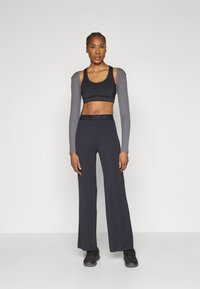 Svart atletisk cropped topp med grå lange ermer, kombinert med mørke vide bukser. Teksturert stoff og subtil logo på linningen.