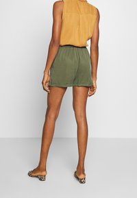 Olivgröna shorts med elastisk midja, tillsammans med en ärmlös topp i senapsgul färg. Djurmönstrade klackskor fulländar stilen.