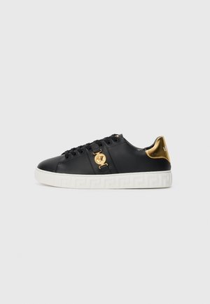 Sneakers en cuir noir avec des accents dorés, ornement de logo et semelle blanche à motifs. Présente des lacets ronds et un design épuré.