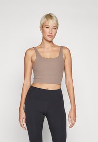 Top cropped castanho com textura canelada, apresentando um decote em scoop e alças largas, combinado com leggings pretas de cintura alta com costuras em contraste.