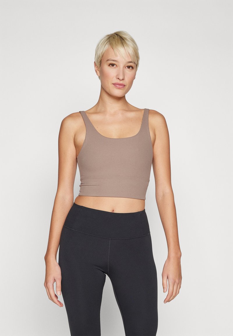 Top cropped castanho com textura canelada, apresentando um decote em scoop e alças largas, combinado com leggings pretas de cintura alta com costuras em contraste.
