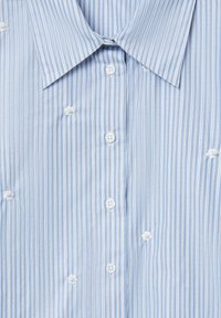 Camicia azzurra chiaro con righe bianche verticali, dotata di piccoli bottoni a forma di fiore e un design del colletto classico.