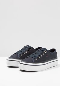 Marina tygsneakers med vit plattformssula, guldöglor och blå snören. Har en liten logopatch på sidan.