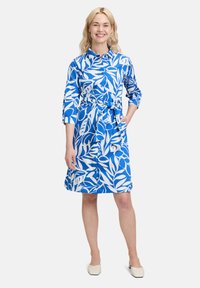 Abito floreale blu e bianco con maniche lunghe, chiusura a bottoni frontale, cintura in vita e vestibilità comoda. Tessuto liscio con un motivo vivace.