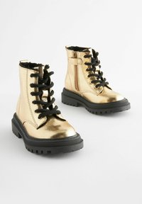 Metallisch goldene Knöchelstiefel mit schwarzen Schnürsenkeln, seitlichem Reißverschluss und schwarzen Gummisohlen. Glatte Textur und klobiges Design mit profilierten Sohlen.