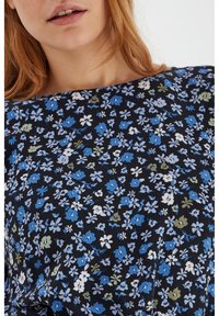 Květinová blůza s černým pozadím, zdobena malými modrými, bílými a zelenými květinami. Lehká tkanina, kulatý výstřih a krátké rukávy.