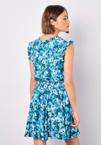 Blumenkleid in Blau- und Grüntönen, mit Rüschensäumen, tailliertem Schnitt und ausgestelltem Rock. Glatte Stofftextur.