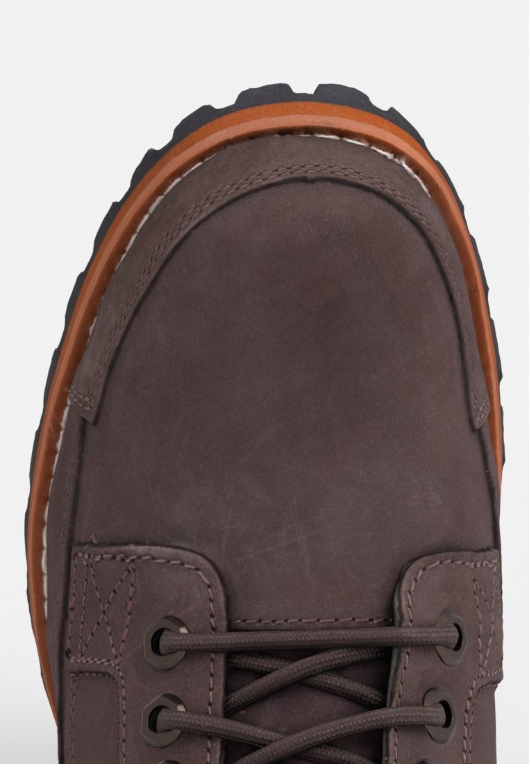 Zapato de cuero marrón con punta redondeada, suela de goma y ribete naranja. Presenta cordones y costuras visibles a lo largo de los lados.