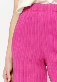 Roze textuurbroek met een ribbelpatroon, voorzien van een elastische tailleband voor flexibiliteit. De stof lijkt lichtgewicht en comfortabel.
