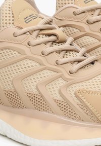 Beżowe buty sportowe z siateczkową cholewką, wzmocnionymi nakładkami, teksturowanymi akcentami oraz sznurowanym designem z miękką, jasną podeszwą.