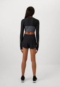 Black long-sleeve crop top with a gray panel, paired with black shorts. The outfit features a comfortable fit and smooth, stretchy fabric.
