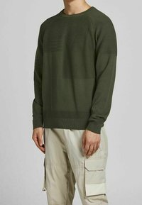 Pull en maille vert olive avec une texture côtelée horizontale sur les épaules et la poitrine, doté d'un col rond ainsi que de poignets et d'un bas en côtes.