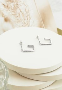 Silver geometriska örhängen med en rektangulär form som har en rad små klara rhinstenar längs en kant, polerad yta.