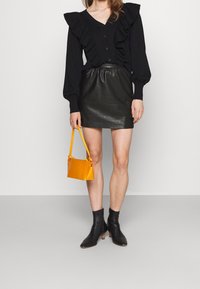 Black ruffled blouse with buttons, black leather mini skirt, yellow handbag, and black heeled ankle boots. Smooth textures and contrasting colors.