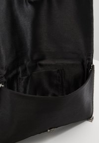 Schwarzes Satin-Handtascheninnere mit glatter Textur, das eine kleine Tasche und silberne Hardware-Akzente für den Verschluss aufweist.