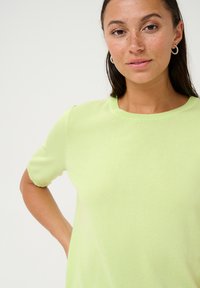 Top cu mânecă scurtă, de culoare verde deschis, dintr-un material tricotat moale, cu guler rotund, siluetă ajustată, textură netedă, design minimalistic.