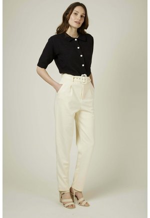 Pull noir à manches courtes avec un col et des boutons en forme de fleur, associé à un pantalon crème taille haute avec une large ceinture et des plis.