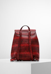 Punainen käärmekuvioinen reppu, jossa on teksturoidu viimeistely, säädettävät olkaimet ja yläkahva. Pääosastossa on läppäkiinnitys.