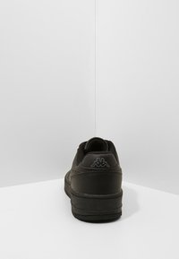 Black sneaker with a smooth leather upper, round toe, padded collar, and textured rubber sole; features a logo on the heel.