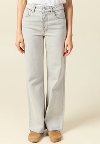 Jeans de tiro alto en gris claro con pierna ancha, confeccionados en denim; diseño de cinco bolsillos con cremallera y detalles de costura.