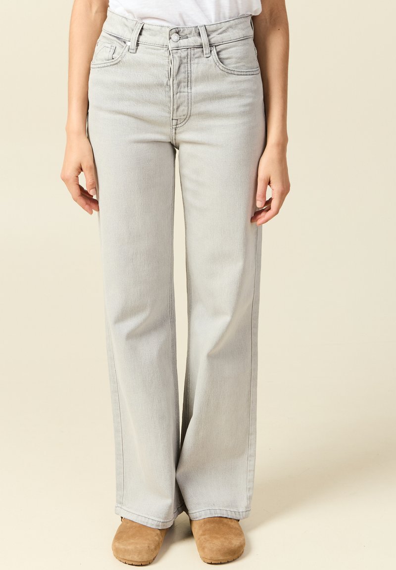 Jeans de tiro alto en gris claro con pierna ancha, confeccionados en denim; diseño de cinco bolsillos con cremallera y detalles de costura.