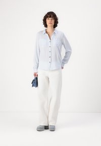 Light blue and white striped button-up shirt with two chest pockets, paired with white wide-leg pants and gray slip-on shoes.
