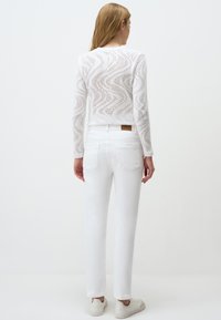 Witte, gebreide trui met een golvenpatroon en lange mouwen, gecombineerd met witte jeans en witte sneakers, gezien van achteren.