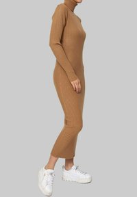 Robe à col roulé à manches longues côtelées de couleur beige clair, silhouette ajustée, longueur mi-mollet, accompagnée de baskets blanches épaisses.