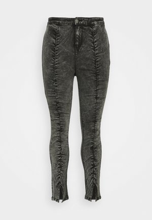 Sorte højtaljede skinny bukser med rynkede lodrette syninger og slidser foran ved anklerne, med knap- og lynlåslukning.