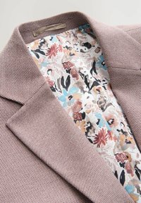 Texturiertes, hellrosa Blazerjacke mit Reverskragen; Futter mit Blumenmuster in sanften Farben, mit Akzenten in Blau, Rosa und Braun.