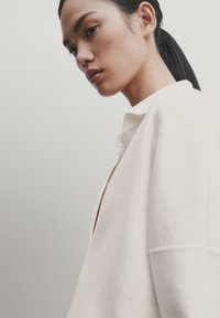 Veste en coton mélangé blanche à coupe décontractée, avec un col et une texture subtile, présentée en vue de côté.