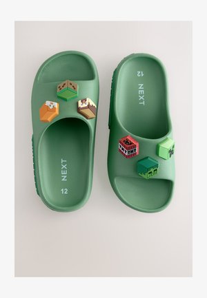 Grüne Plastik-Sandalen mit strukturiertem Fußbett, versehen mit vier bunten, abnehmbaren Blöcken oben, darunter pixelige Designs aus einem Videospiel.