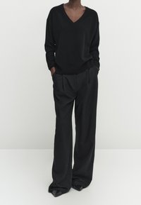Black V-neck sweater with long sleeves paired with loose black trousers and pointed-toe black shoes. Smooth texture, minimalist design.