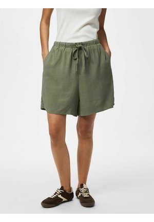 Shorts vert olive à cordon, portés avec un haut blanc sans manches et des baskets marron aux lacets blancs, mains dans les poches, sur un fond uni.