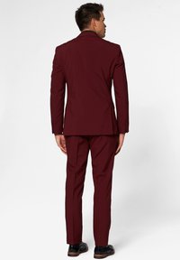 Burgundský oblek so slim-fit strihom, nohavicami s plochým predným dielom a zodpovedajúcim blejzrom. Vyrobený z hladkého materiálu; obsahuje precízne šitie a akcenty na gombíky.