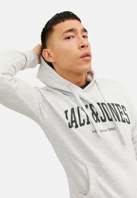 Lys gr�å hættetrøje med en frontlomme, snore og en sort logo tekst "JACK & JONES" med "est. siden 1990" trykt nedenfor.