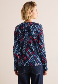 Langmouwshirt in een marineblauwe stof met een geometrisch patroon in tinten lichtblauw en rood. Ronde halslijn en een ontspannen pasvorm.