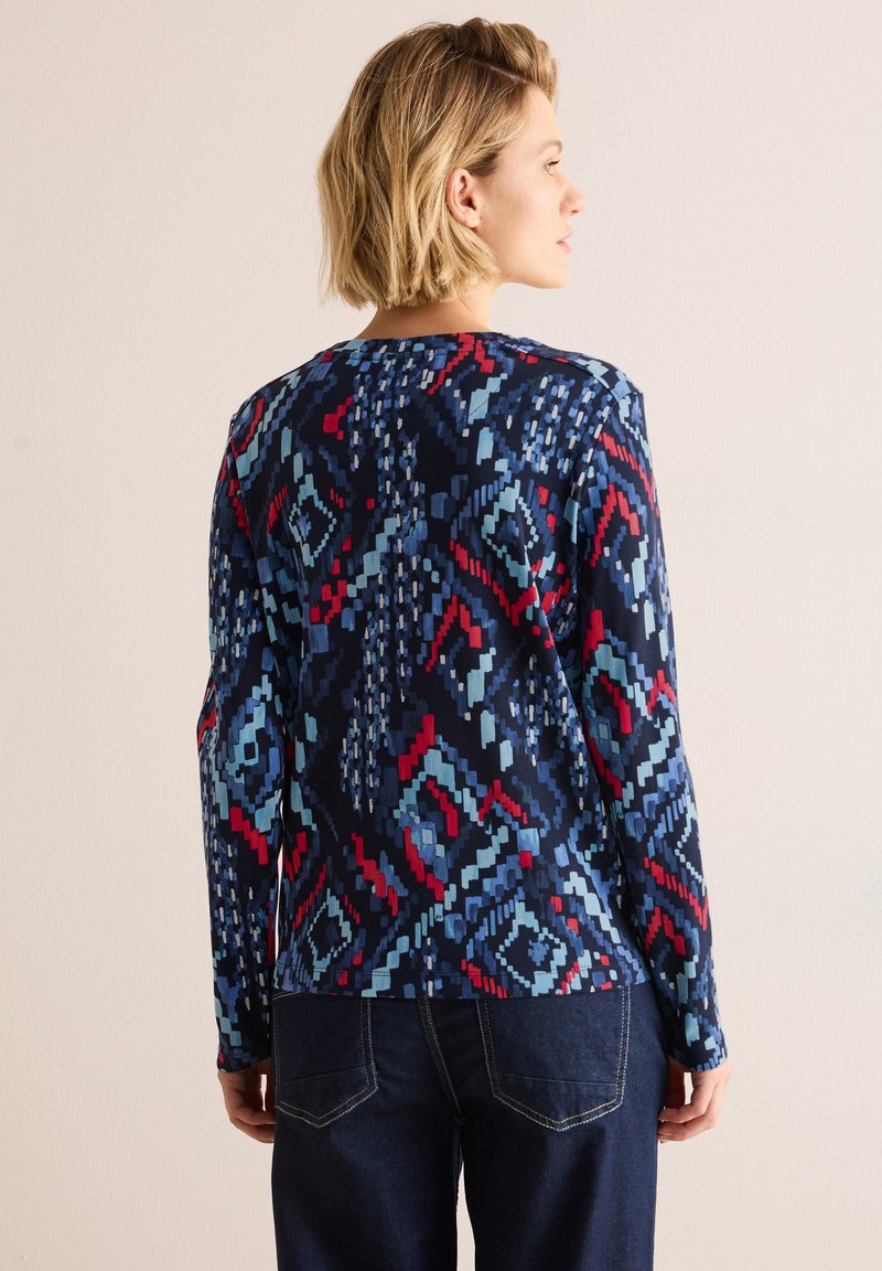 Langmouwshirt in een marineblauwe stof met een geometrisch patroon in tinten lichtblauw en rood. Ronde halslijn en een ontspannen pasvorm.
