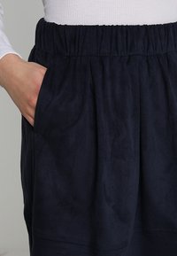 Marineblauwe rok met elastische tailleband, gemaakt van zachte, gestructureerde stof, met zijzakken en een relaxte pasvorm. Duidelijke plooien bij de taille.