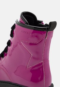 Botín de tobillo de charol rosa con cordones negros, que presenta un diseño de estrella y el logotipo de Geox. Textura suave con costuras en contraste.