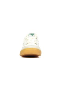 Witte sneakers met een gestructureerd ontwerp en groen logo. Beschikt over een gumzool en geperforeerde details aan de zijkanten voor ademend vermogen.